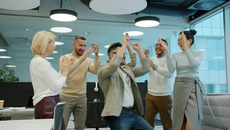 עובדים חוגגים יחד באירוע במשרד מודרני, רוקדים ומוחאים כפיים